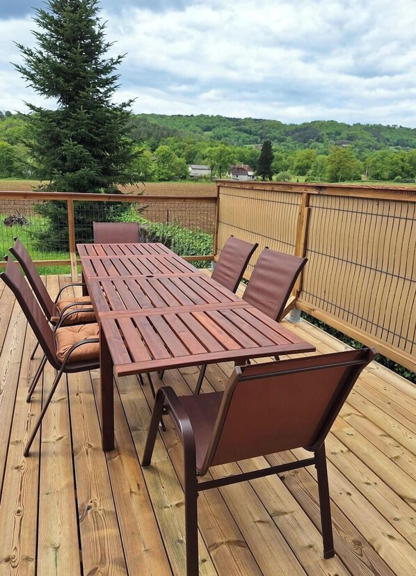 Eine Holzterrasse mit Tisch und Stühlen, umgeben von einem Bambuszaun, mit Blick auf eine grüne Landschaft.