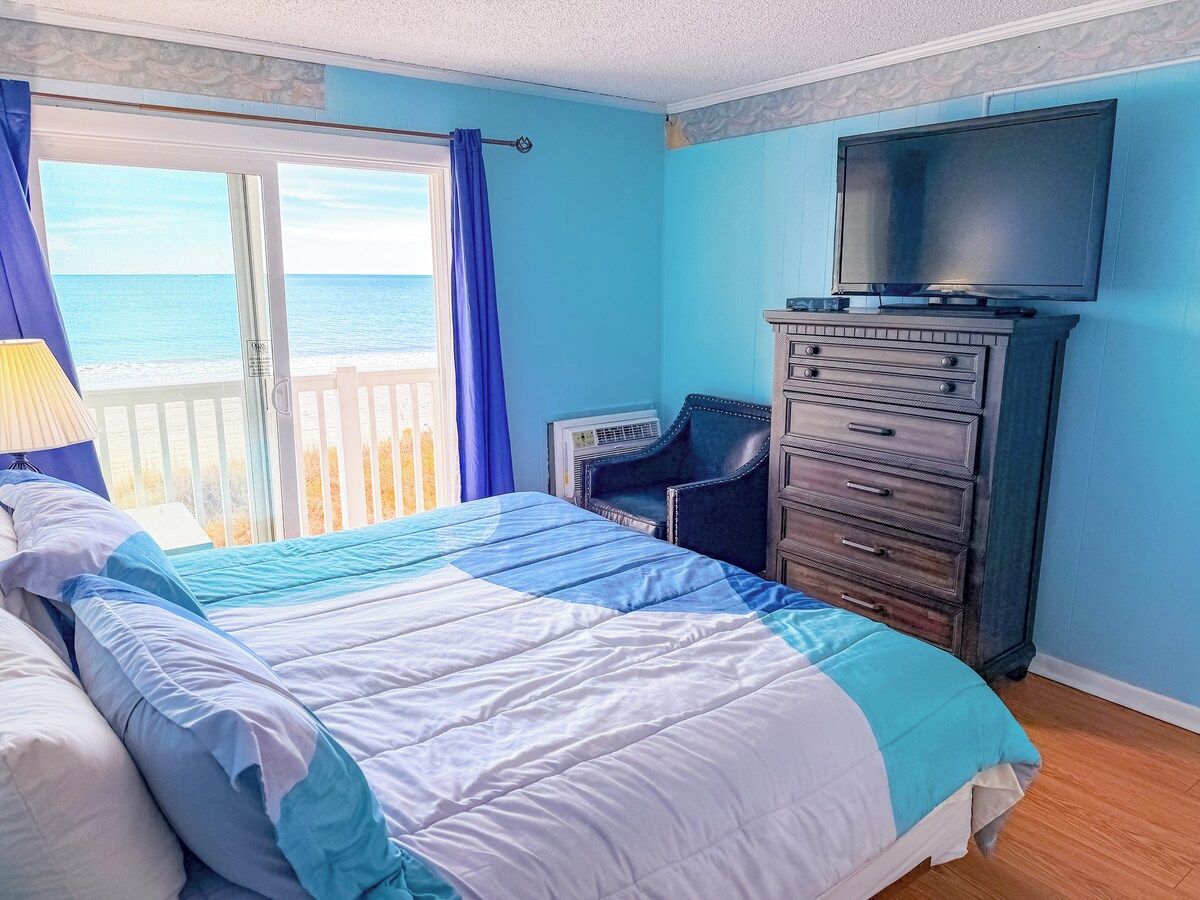 Une chambre à coucher avec un lit, une commode, un téléviseur et une vue sur l’océan.