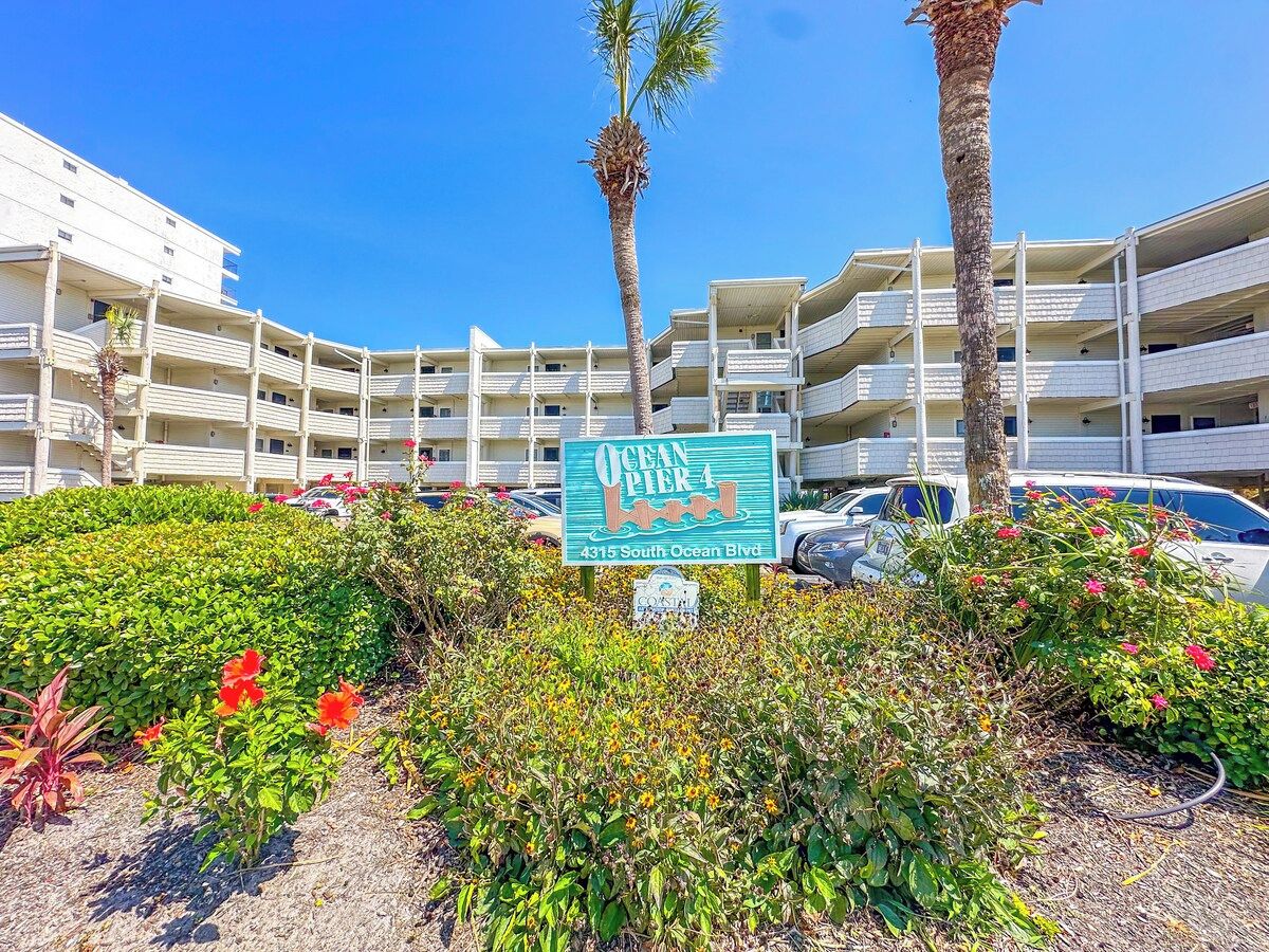 A multi-story hotel with a sign indicating 'Ocean Pier 4' and a parking lot in front.