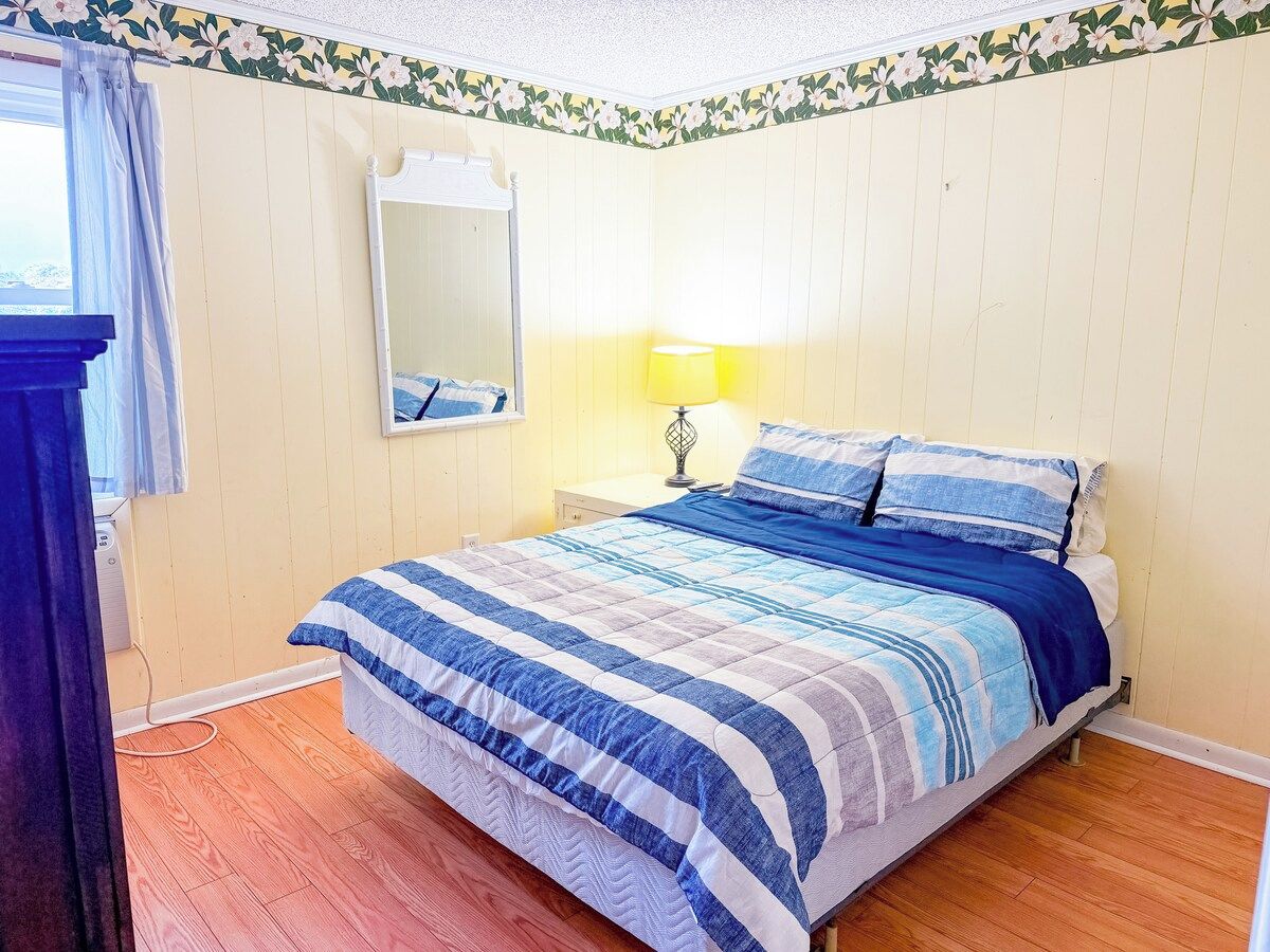 Une chambre à coucher avec un lit, une lampe de chevet, un miroir et une fenêtre avec des rideaux.