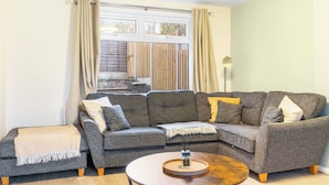 A living room with a grey sectional sofa, a small round coffee table, and a window with curtains. - Stylsih 3BR House - Sleeps 5 - Near City Centre - Free Parking (Leeds)