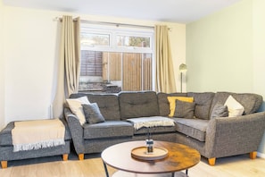 A living room with a grey sectional sofa, a small round coffee table, and a window with curtains.
