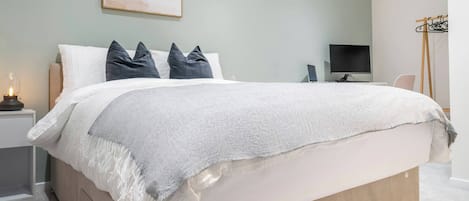 A neatly arranged bedroom with a bed, bedside table, TV, and a coat rack.