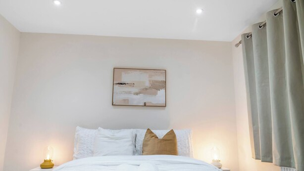 A hotel room with a neatly made bed, a bedside table with a lamp, and a painting on the wall. - Stylsih 3BR House - Sleeps 5 - Near City Centre - Free Parking (Leeds)