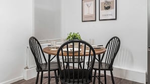 A dining area with a round table, four black chairs, two framed pictures on the wall, and a potted plant. - Stylsih 3BR House - Sleeps 5 - Near City Centre - Free Parking (Leeds)