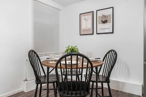 A dining area with a round table, four black chairs, two framed pictures on the wall, and a potted plant.