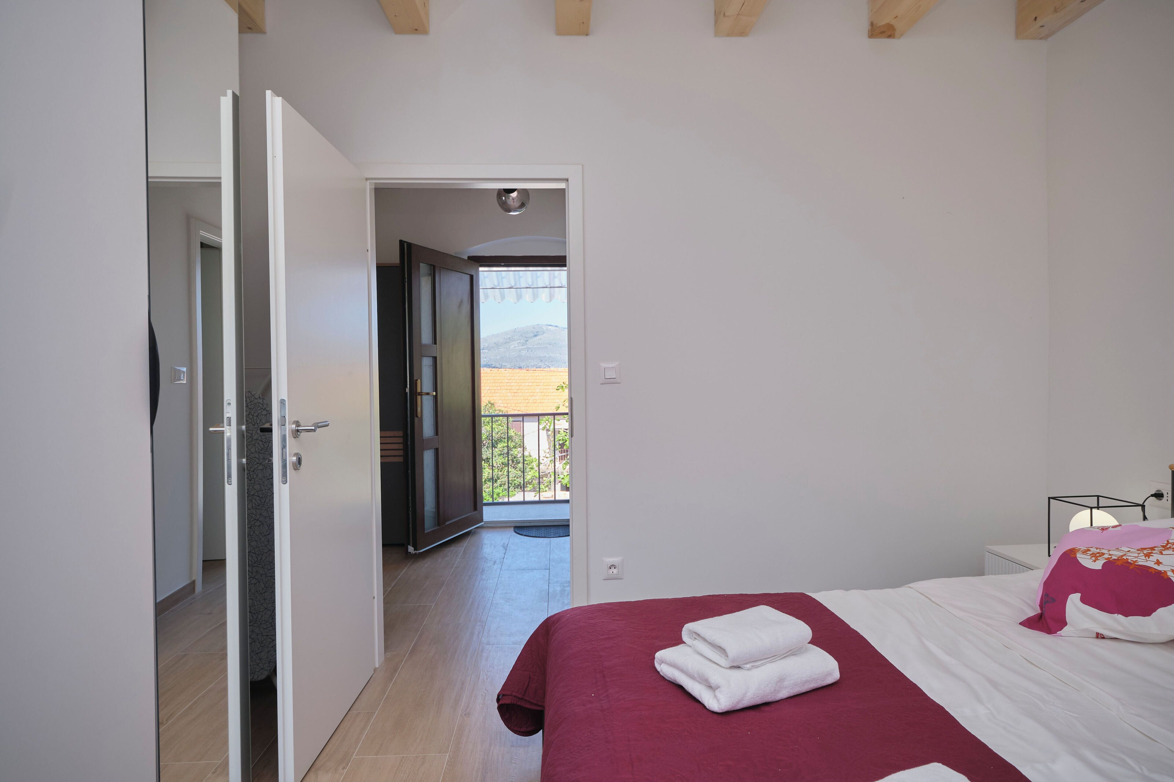 Een slaapkamer met een bed, uitzicht op een balkon en een deur naar een andere kamer.