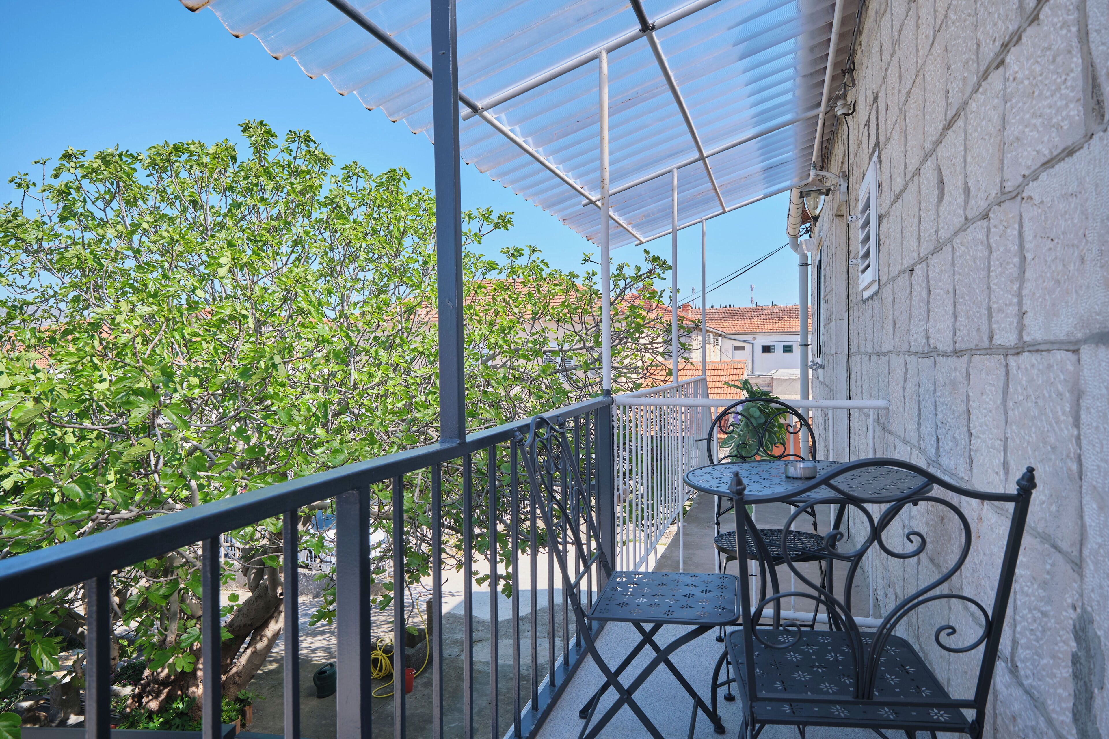 A balcony with a metal railing, a table with chairs, and a view of trees and buildings.