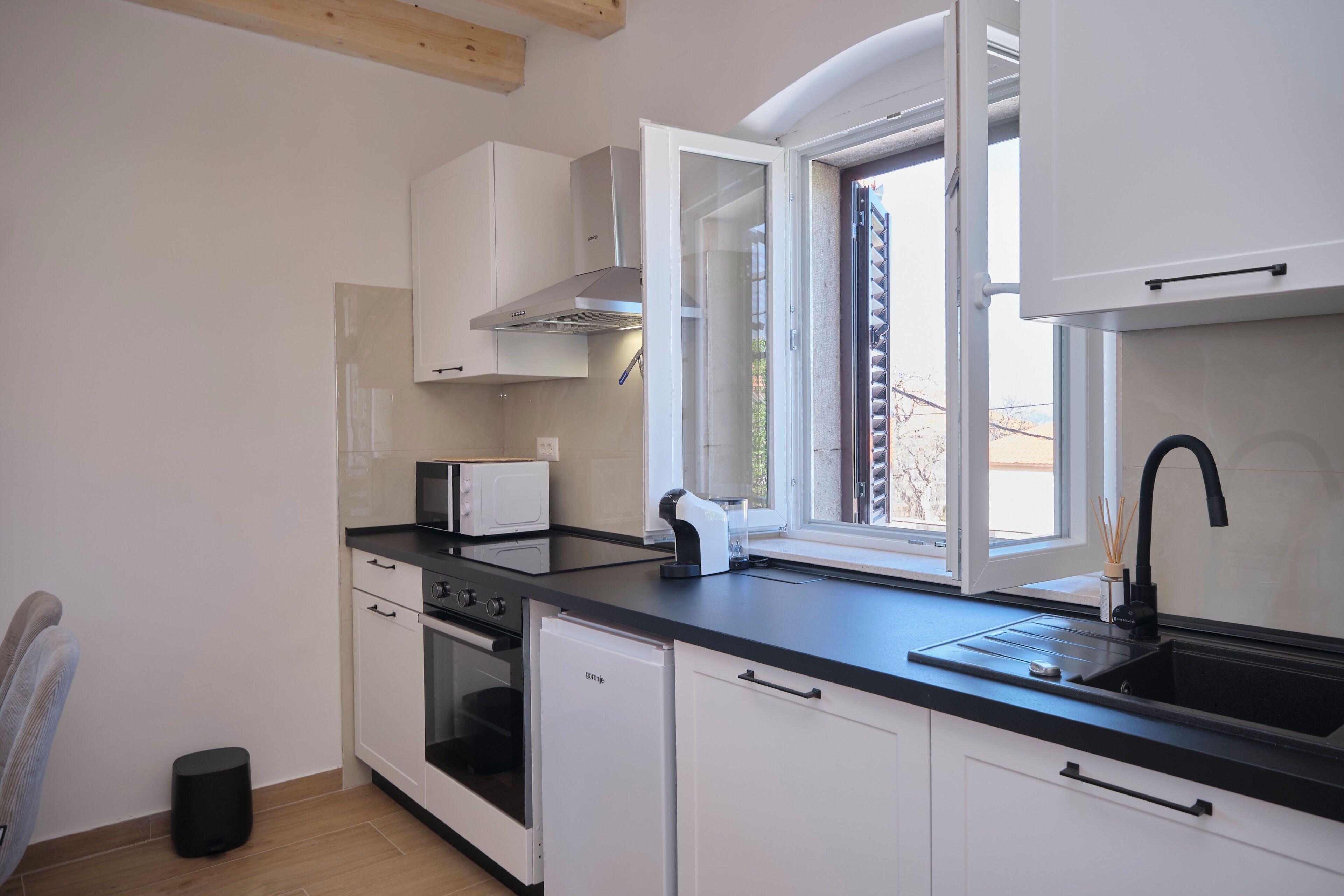 A modern kitchen with white cabinets, a black countertop, a built-in oven, a microwave, a sink, and a window with a view of the outdoors.
