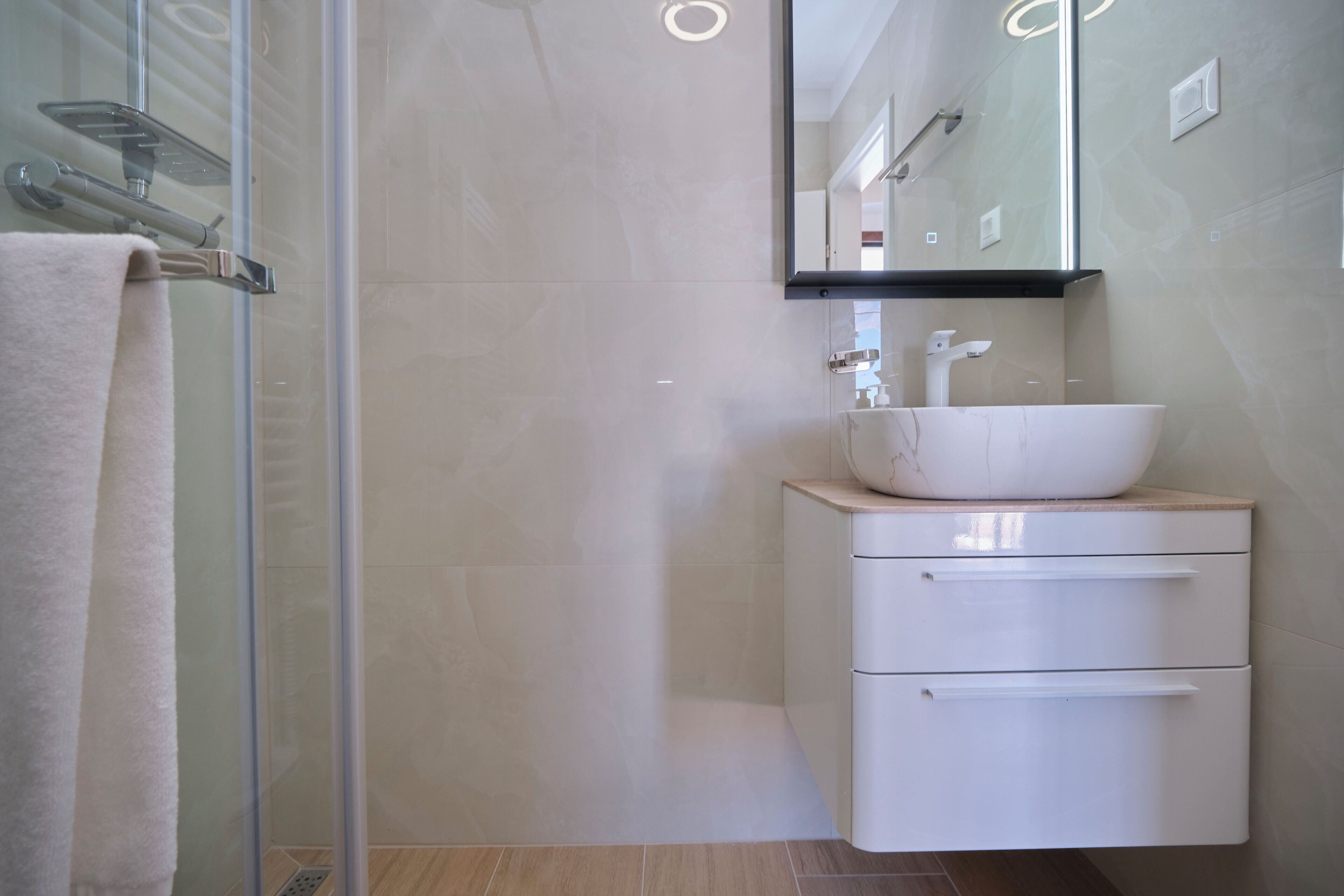 Un bagno moderno con cabina doccia in vetro, un lavabo bianco con piano in marmo e uno specchio sopra il lavabo.