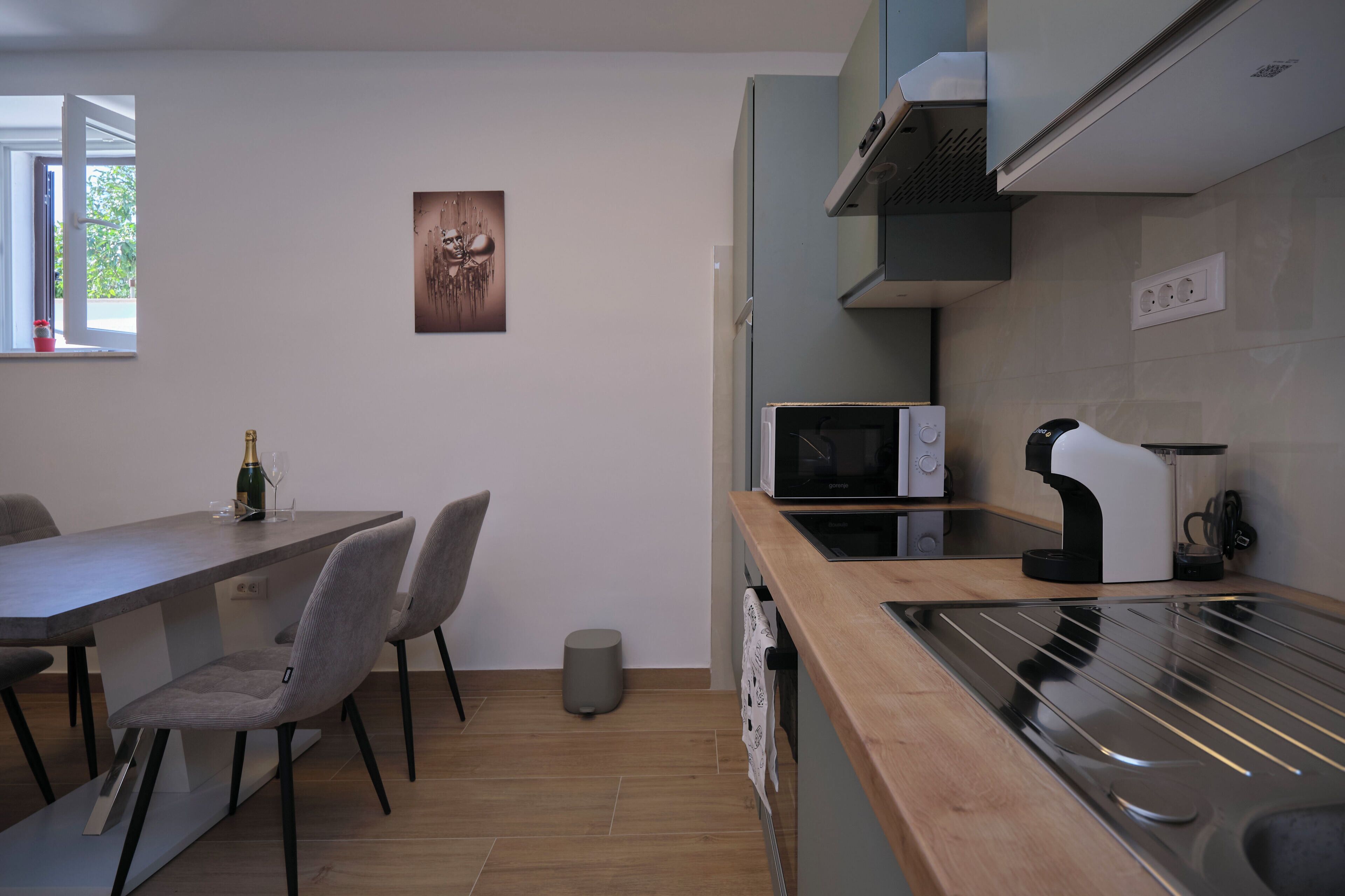 A modern kitchen with a microwave, coffee maker, and a sink. There is a dining table with chairs and a trash can.