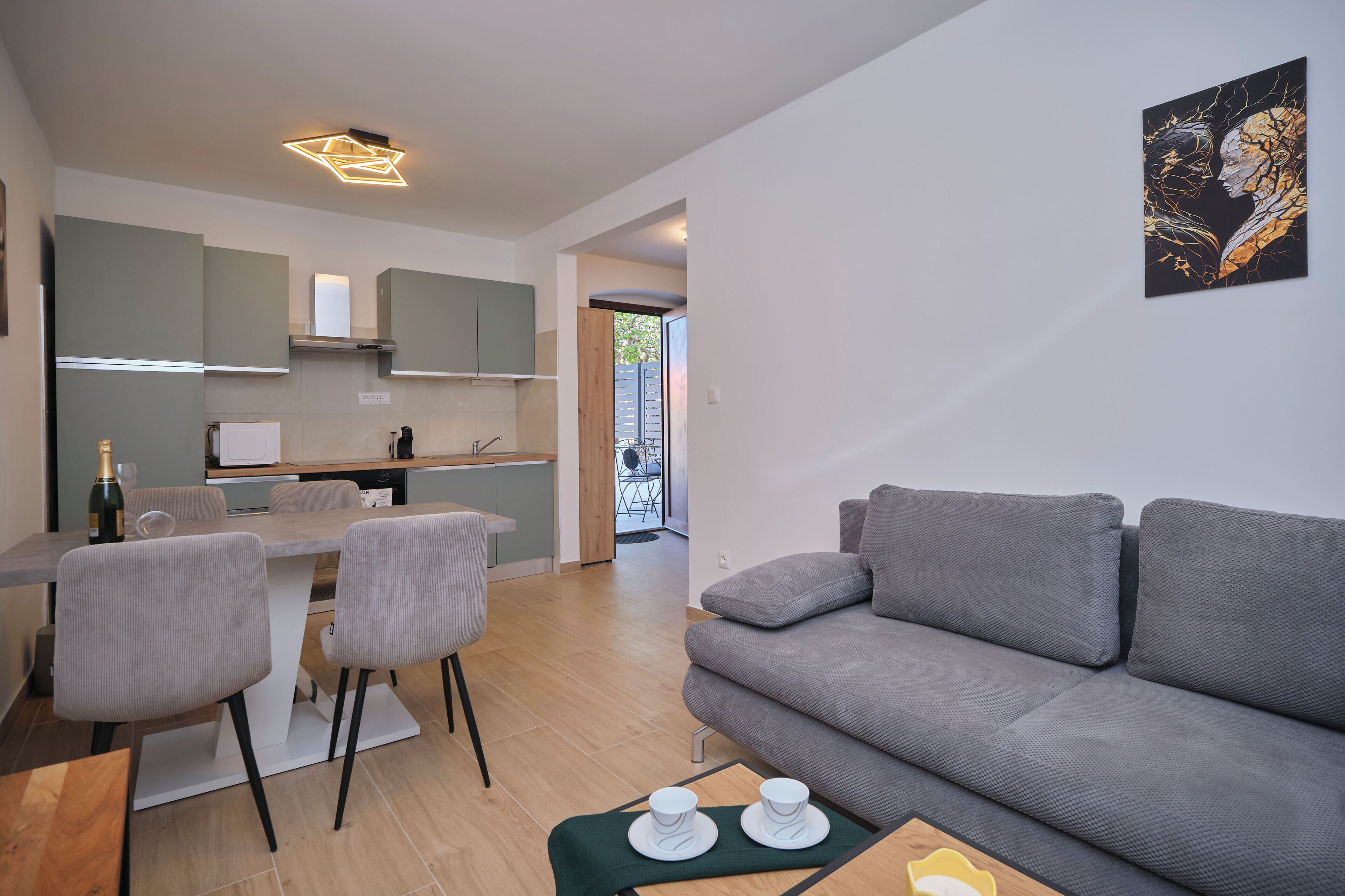 Una sala de estar moderna con un sofá gris, un comedor con sillas, una cocina con armarios y un cuadro en la pared.