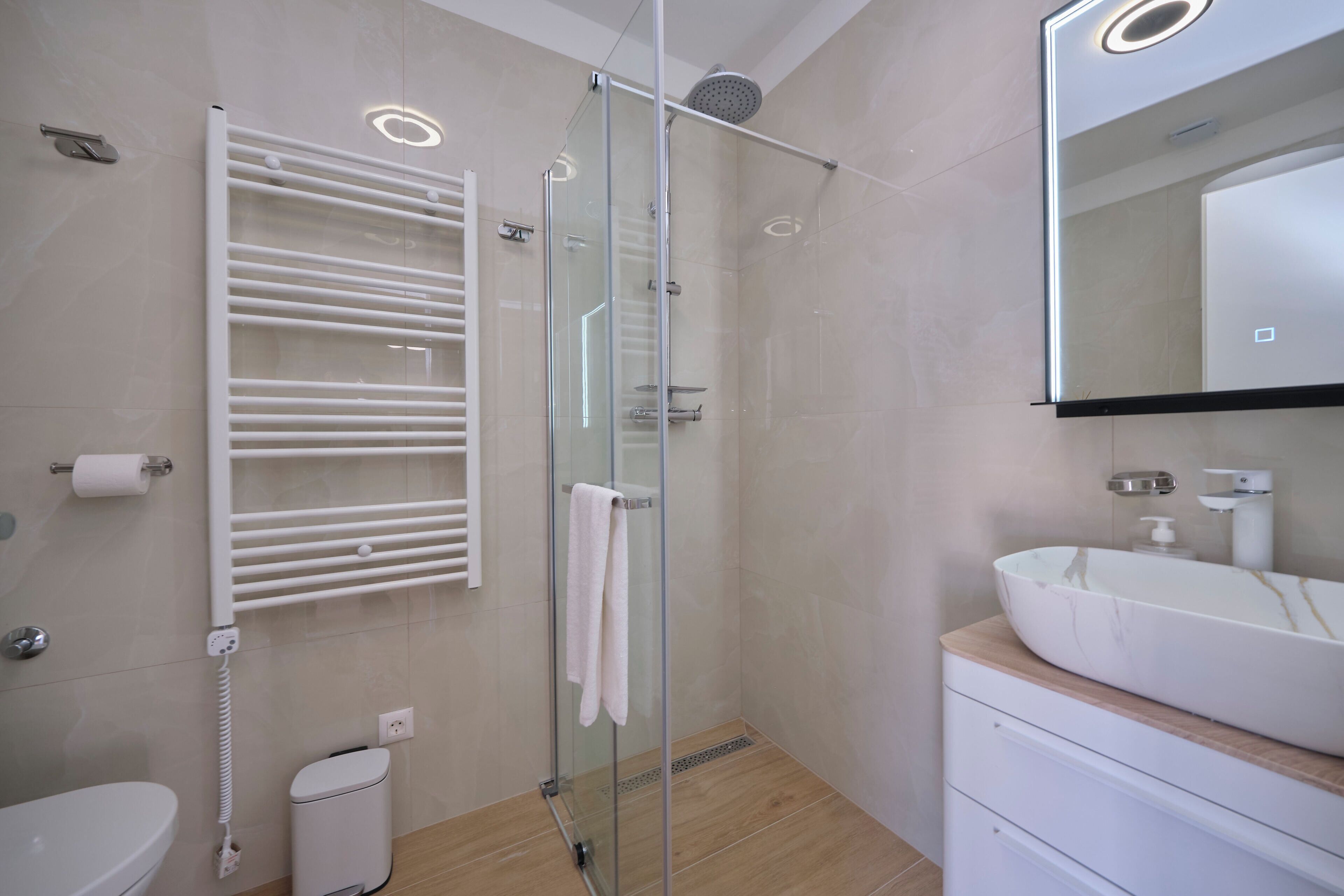 A modern bathroom with a glass-enclosed shower, a white sink, and a towel rack.
