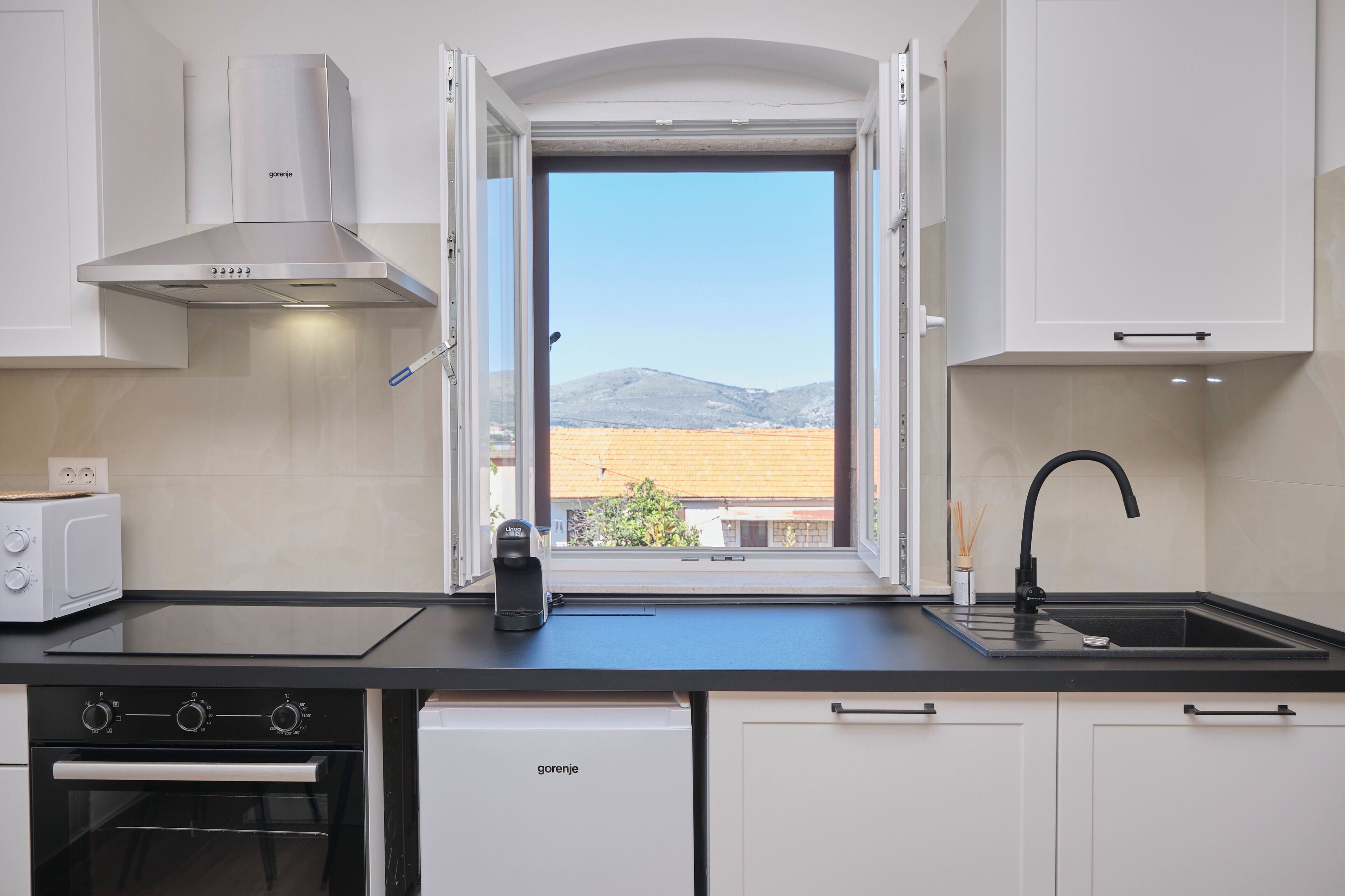 A kitchen with a view of a mountain, a coffee maker, and a modern stove.