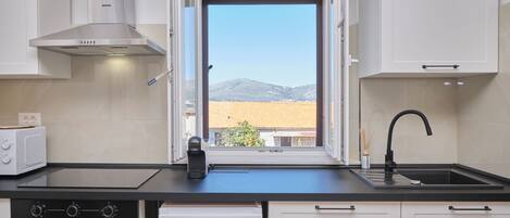 A kitchen with a view of a mountain, a coffee maker, and a modern stove.