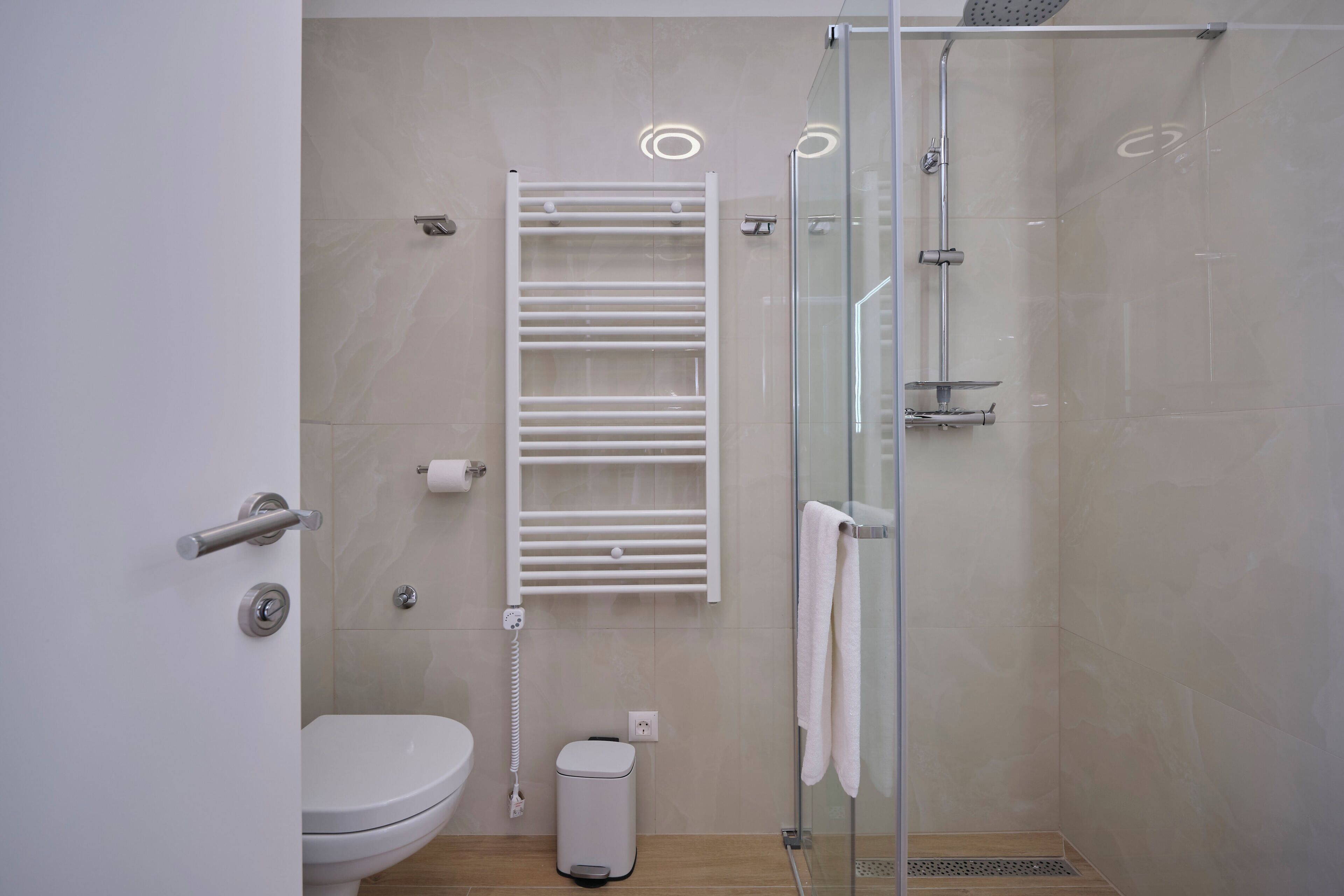 Une salle de bain moderne équipée de toilettes, d’une douche à parois de verre, d’un porte-serviettes et d’une poubelle.