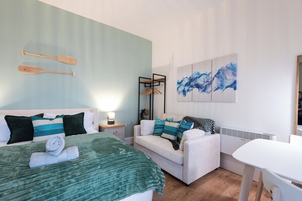 A bedroom with a bed, a sofa, a table, and artwork on the wall.