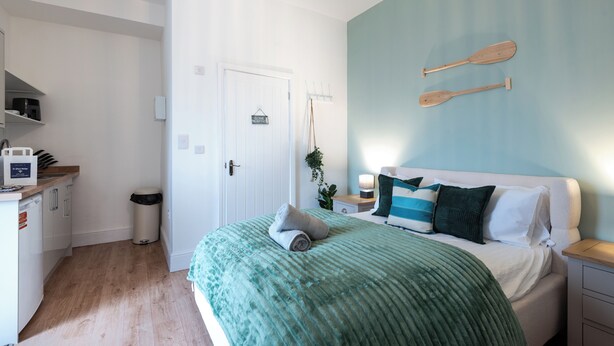 Ein Schlafzimmer mit einem Bett, Kissen, einem an der Wand befestigten Holzschläger, einem kleinen Nachttisch und einem Beistelltisch.