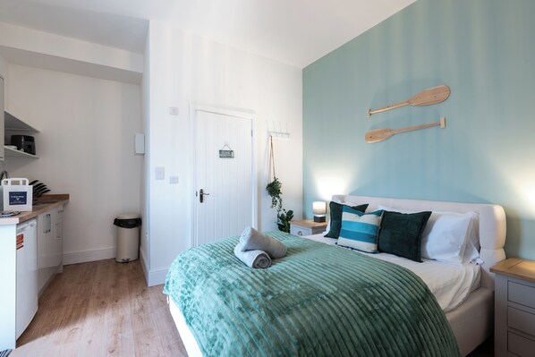 A bedroom with a bed, pillows, a wall-mounted wooden paddle, a small bedside table, and a nightstand.