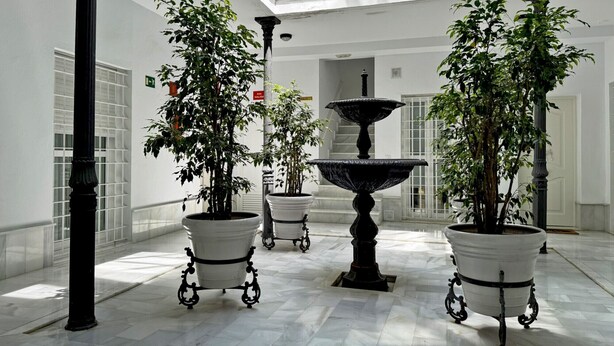 A spacious indoor area with a marble floor, potted plants, a central fountain, and a high ceiling with skylights. - Apartamento Carús - Ole Solutions (Jerez de la Frontera)