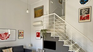 A modern living room with a grey sofa, a striped chair, a wooden table, and a white staircase. - Apartamento Carús - Ole Solutions (Jerez de la Frontera)