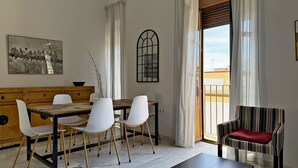 A dining area with a wooden table and white chairs, a striped armchair, a black coffee table, and a window with curtains. - Apartamento Carús - Ole Solutions (Jerez de la Frontera)