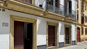 A building with a white facade, a wooden door, and barred windows. - Apartamento Carús - Ole Solutions (Jerez de la Frontera)