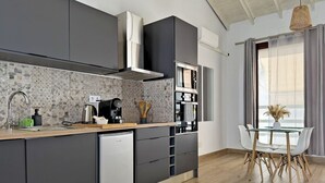 Een moderne keuken met grijze kastjes, een vaatwasser, een koffieapparaat en een eethoek met een glazen tafel en witte stoelen.