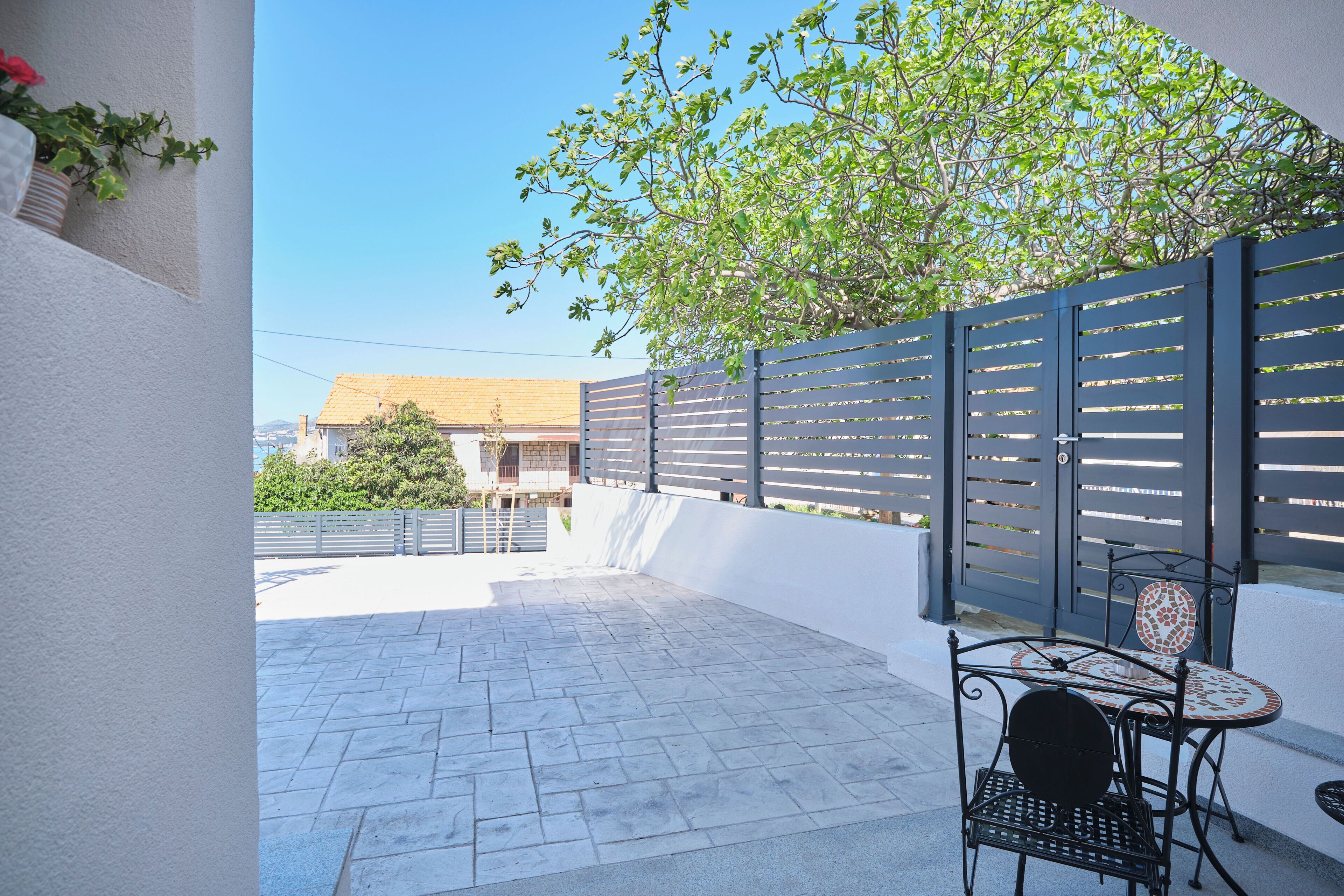 Une terrasse avec une table et des chaises, un pot de fleurs et, en arrière-plan, la vue d’un immeuble.