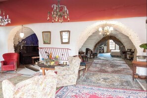 An arched room with a piano, a red armchair, and a patterned sofa.