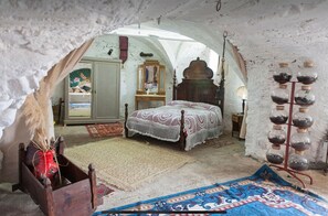 A rustic room with a bed, a wooden cabinet, a mirror, and a collection of glass jars on a shelf.