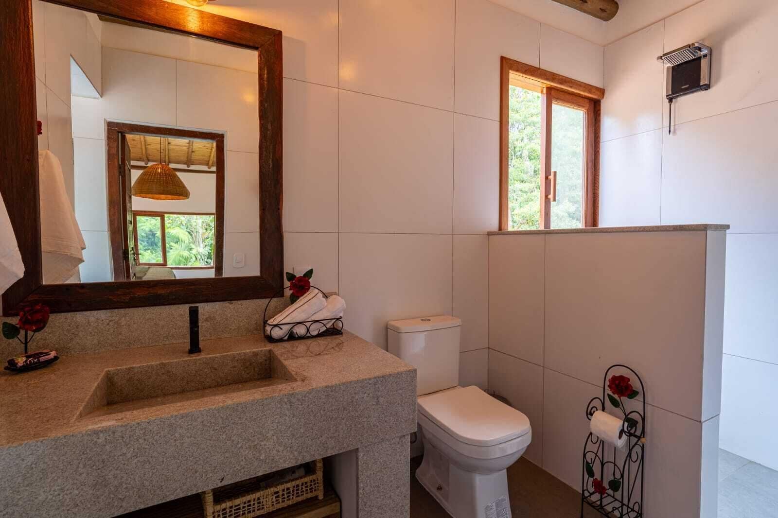 A bathroom with a granite sink, a toilet, a mirror, and a window.