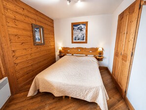 A bedroom with a wooden headboard, a bed with a quilt, wooden walls, a framed picture on the wall, and a wooden door. - Comfortable apartment with clear view - 4 guests (Les Menuires)