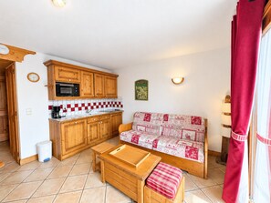 A compact living space with a kitchenette, a sofa, and a wooden table. - Comfortable apartment with clear view - 4 guests (Les Menuires)