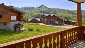 Ein Holzhaus mit Steinunterbau, einem Balkon mit Geländer und einer Bergkulisse.