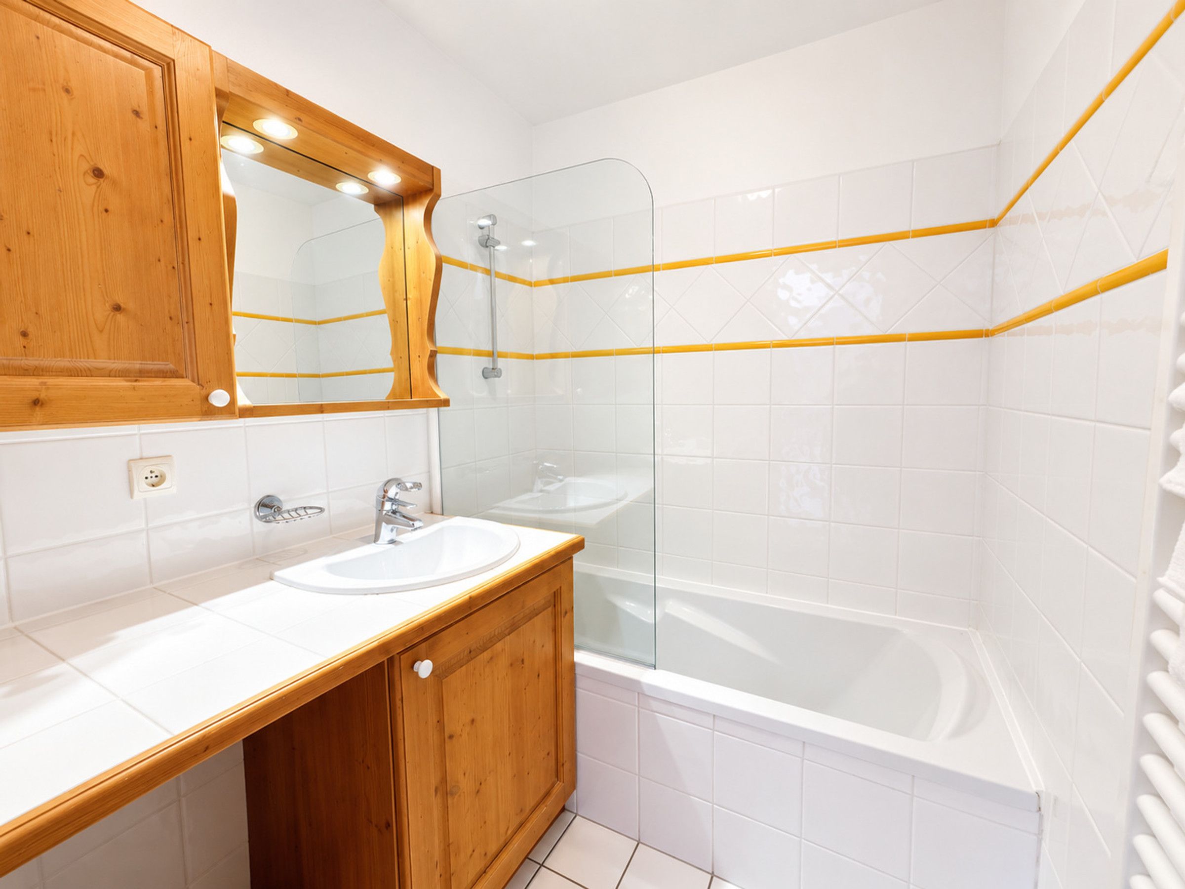 Un baño con tocador de madera, un lavabo blanco, un espejo y una zona de ducha con mampara de vidrio.