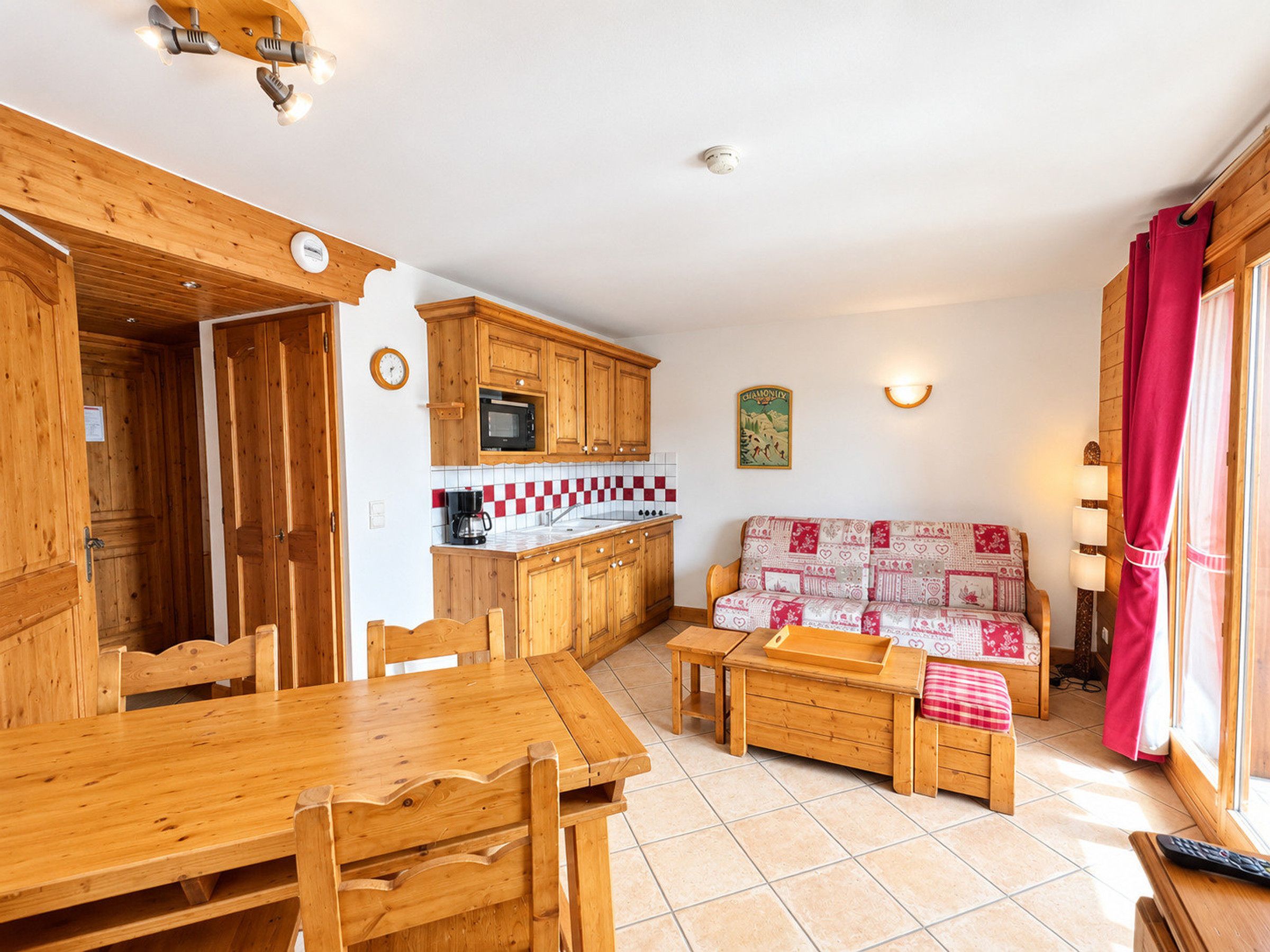 A wooden interior with a dining table, chairs, a sofa, and a kitchen area with wooden cabinets and a microwave.