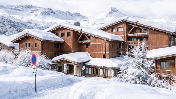 Ein holzhäuschen-artiges Hotel im Chalet-Stil mit mehreren Balkonen, umgeben von schneebedeckten B äumen und Bergen im Hintergrund.