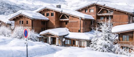 Ein holzhäuschen-artiges Hotel im Chalet-Stil mit mehreren Balkonen, umgeben von schneebedeckten Bäumen und Bergen im Hintergrund.