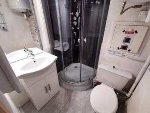 Ett modernt badrum med en dusch som är avskärmad med glasväggar, ett vitt handfat och en toalett.