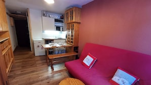 Un espacio habitable compacto con kitchenette, un sofá rojo y un banco de madera.