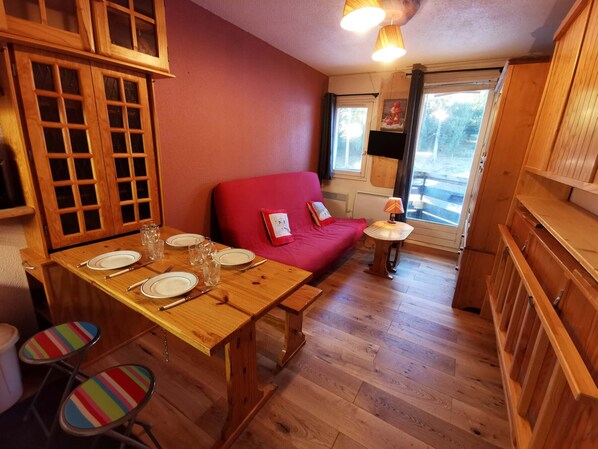Ett mysigt rum med ett matbord i trä som är dukat för fyra personer, en röd soffa och ett litet bord med en lampa.