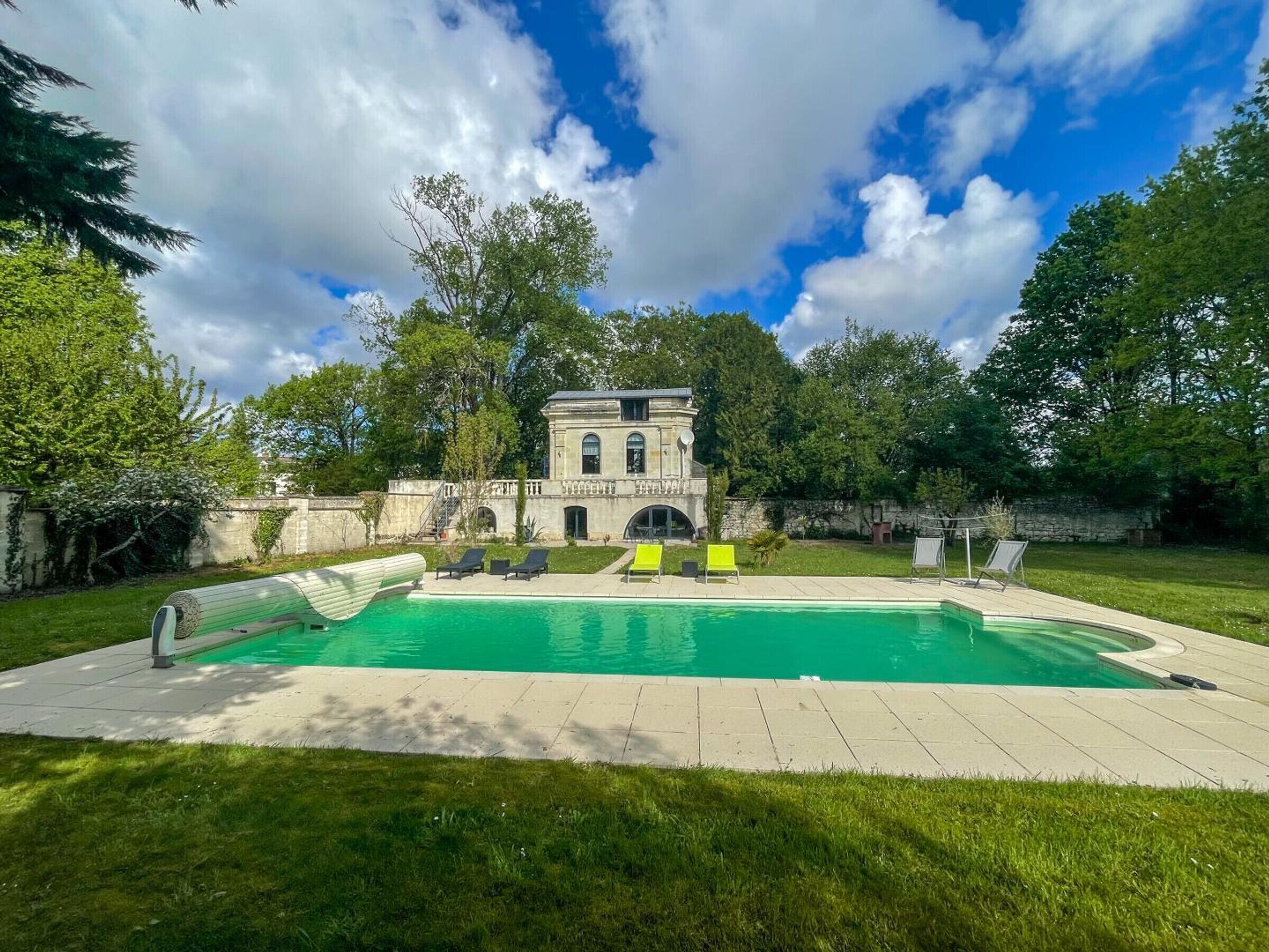 A swimming pool with lounge chairs, a stone building, and surrounding greenery.