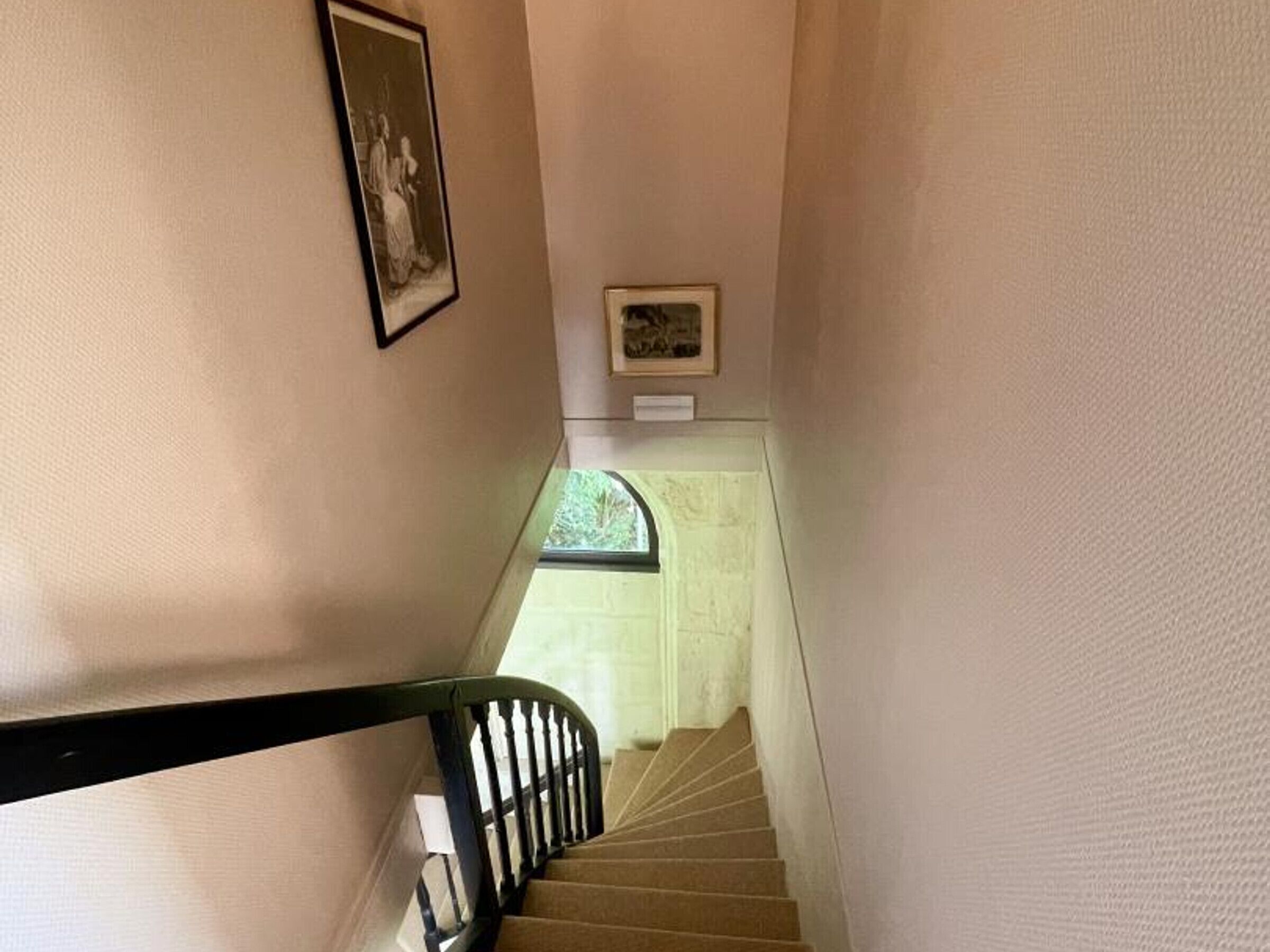 Una escalera estrecha con barandilla negra, un cuadro enmarcado a la izquierda y una pequeña placa en la pared.