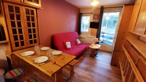 Une pièce chaleureuse avec une table à manger en bois, dressée pour quatre personnes, un canapé rouge et une petite table avec une lampe.