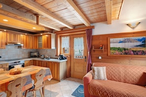 Eine gemütliche Küche mit Holzschränken, einem Esstisch mit Stühlen, einer Couch und einem Gemälde einer Berglandschaft.