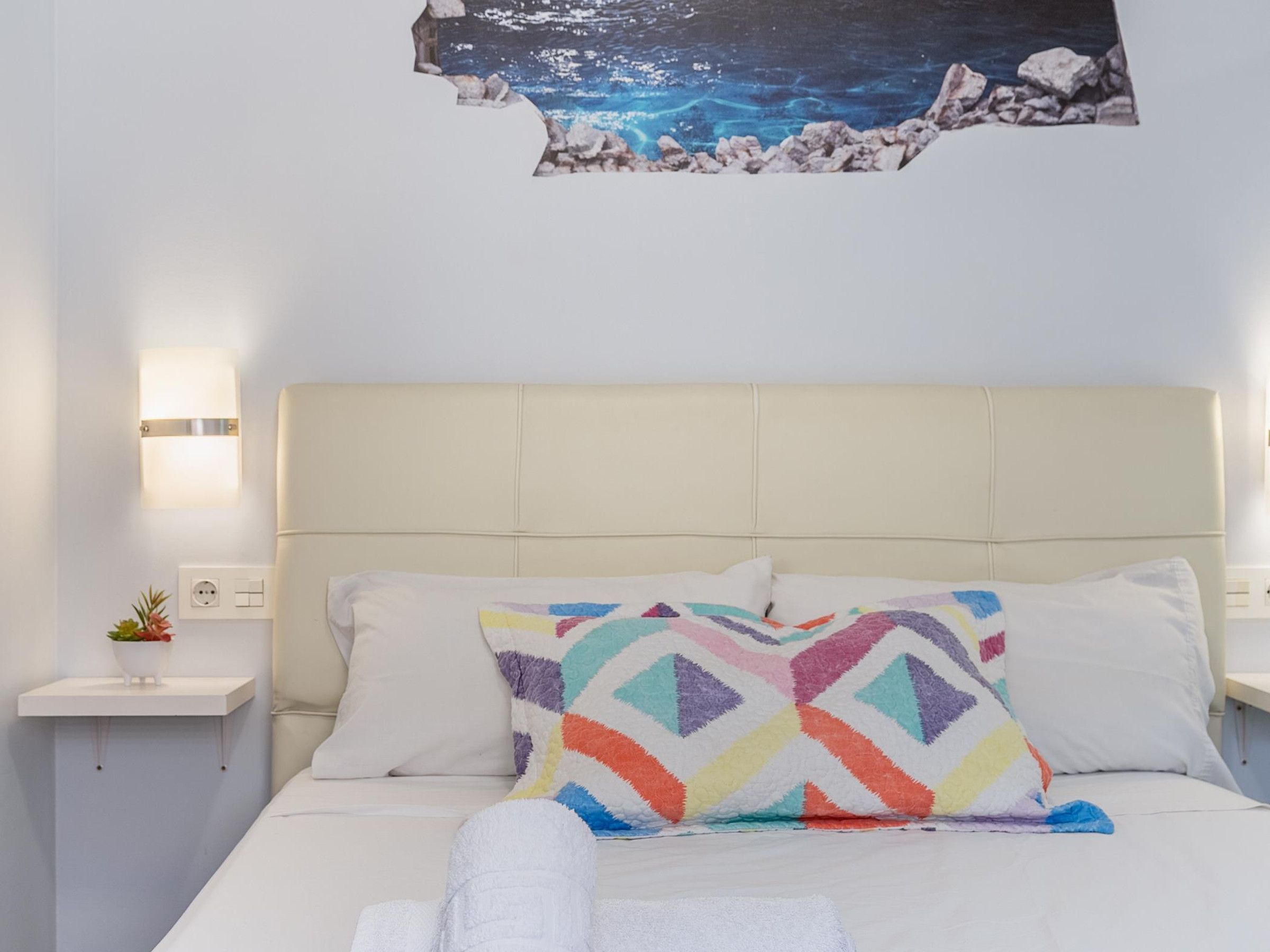 A hotel room with a bed, a nightstand, a wall-mounted light, and a decorative wall piece.