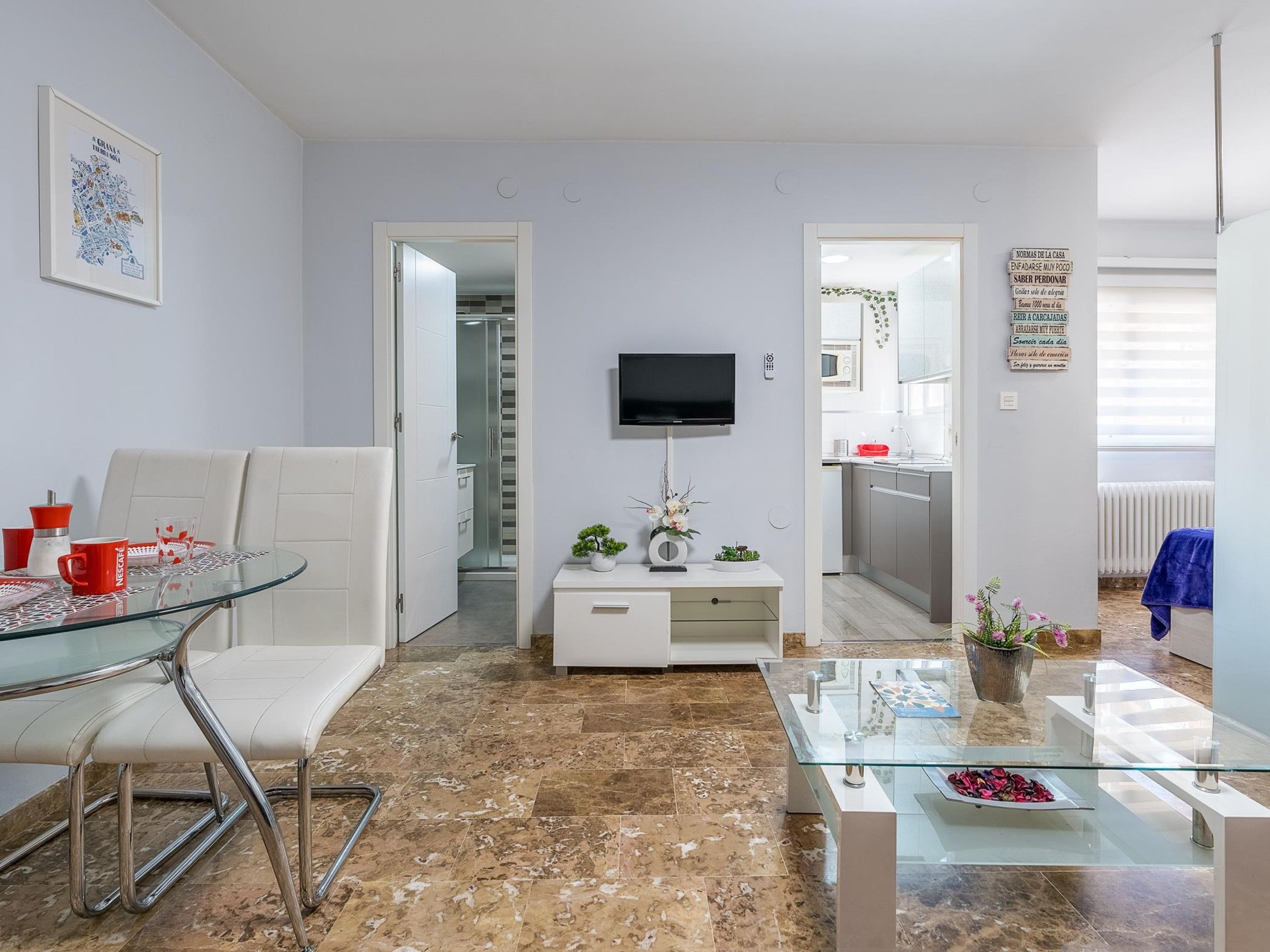 Un salon moderne avec une table basse en verre, un canapé blanc et un téléviseur fixé au mur.