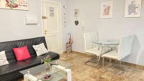 A living room with a black leather sofa, a glass coffee table, white chairs, a glass dining table, and a tiled floor. - Central renovated studio - Stay in Granada (Granada)