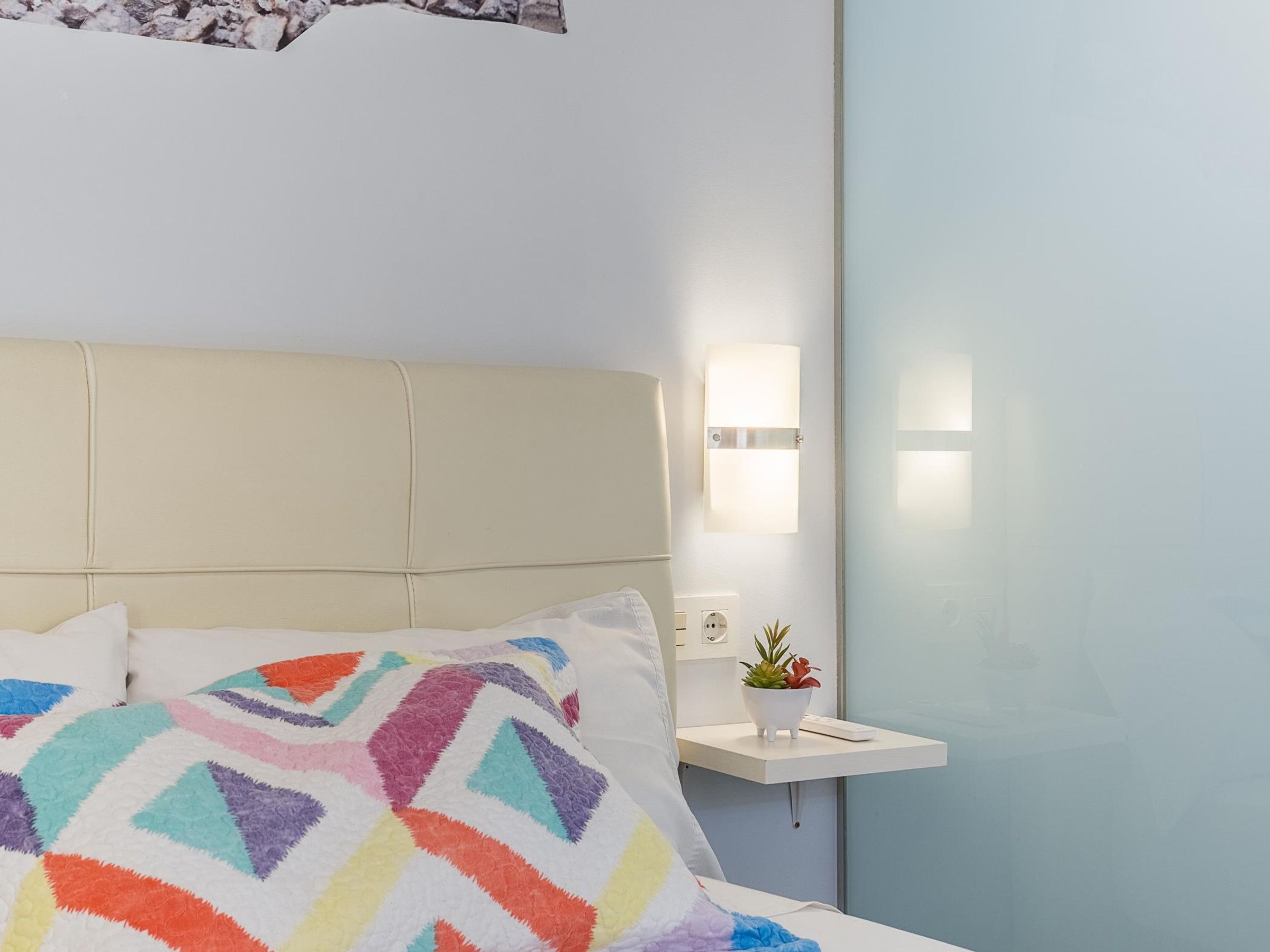 Une chambre d’hôtel avec un lit, une table de chevet ornée d’une plante et un luminaire fixé au mur.